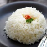 A neatly shaped rice dome of parboiled rice served on a plate with a fork and spoon placed beside it.
