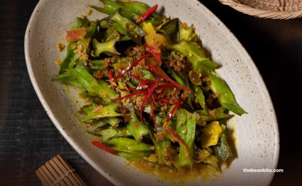 Stir-fried winged beans recipe served in a ceramic bowl, featuring vibrant green star-shaped slices, garnished with red chili strips and crispy shallots Stir-fried winged beans recipe served in a ceramic bowl, featuring vibrant green star-shaped slices, garnished with red chili strips and crispy shallots